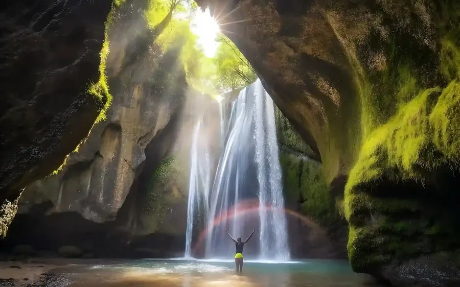 Waterfall falling into a cave lit by a shaft of daylight, inland Bali